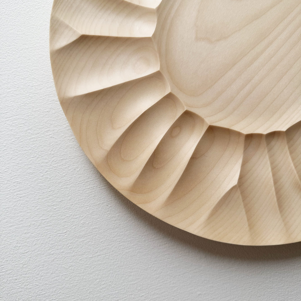 Close up of sycamore wooden plate with a sculptural design on a white background