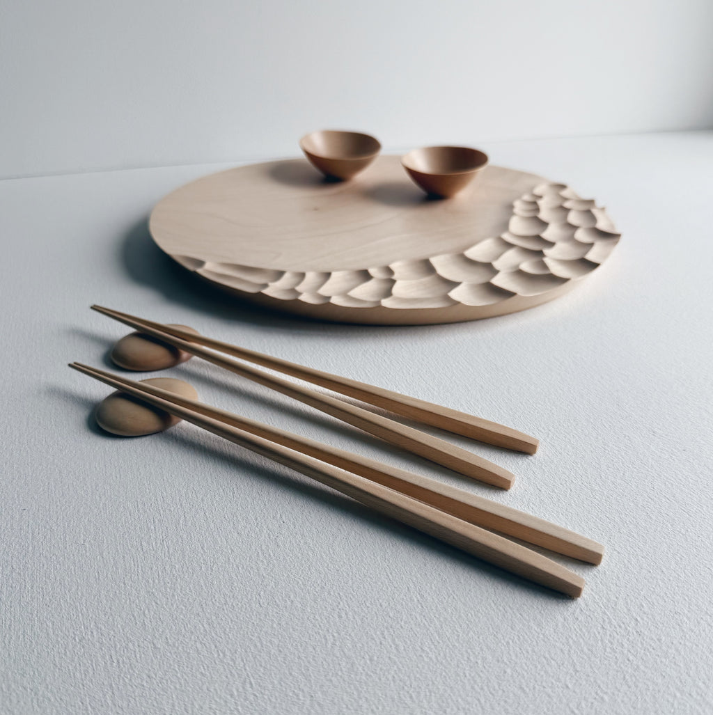 Wooden dining set on circular board with  bowls and chopsticks on a white background