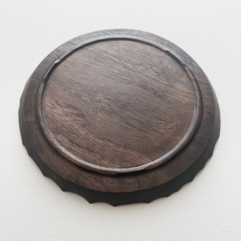 Underside of black walnut coast plate with cratered edge on white background