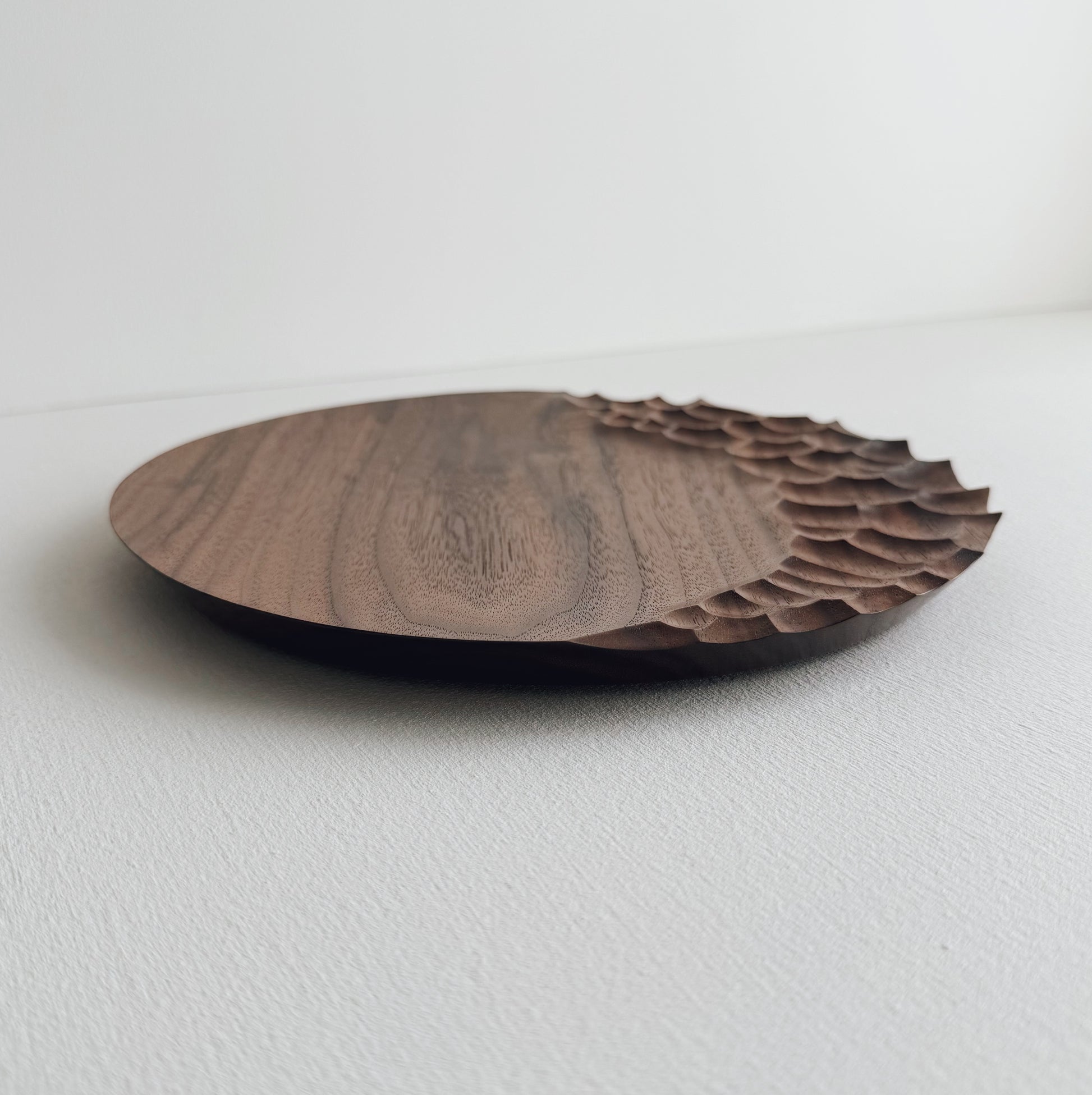 Walnut wooden plate with crater edge design on a white background