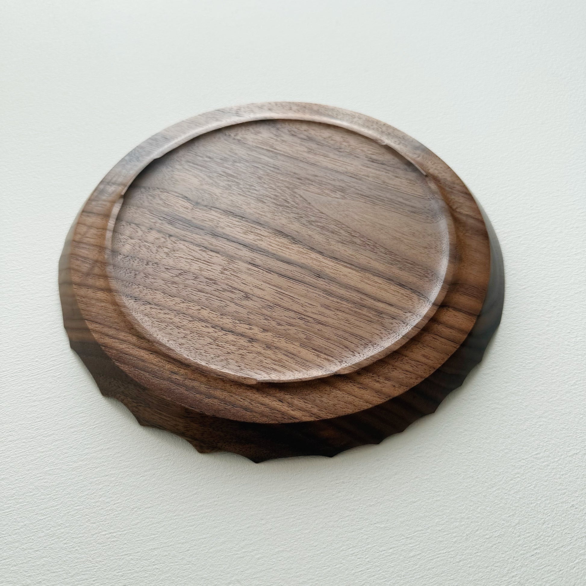 Underneath of walnut wooden plate with crater edge design on a white background