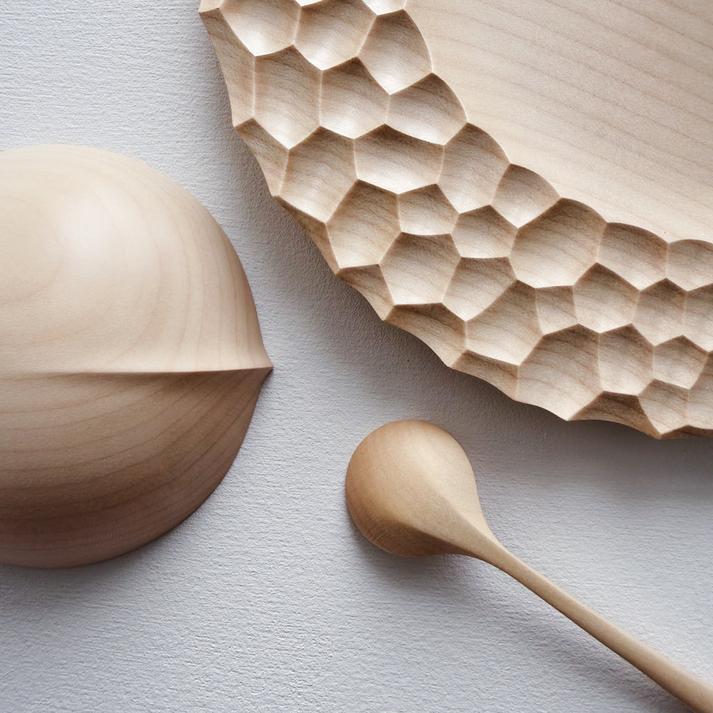 Close up of sycamore wooden plate with craters design, bowl and eating spoon on a white background
