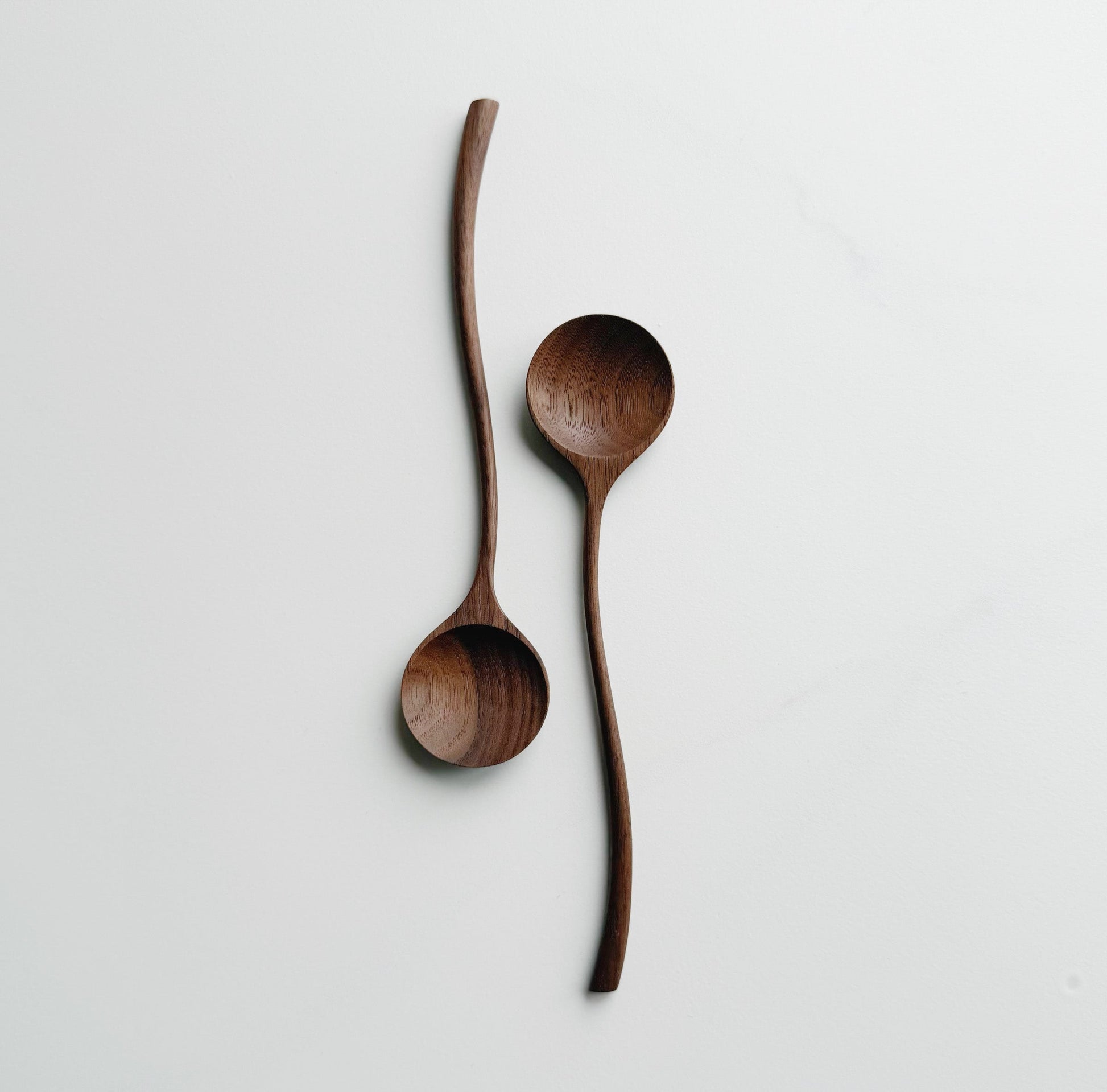 Two walnut curvy spoons on a light background