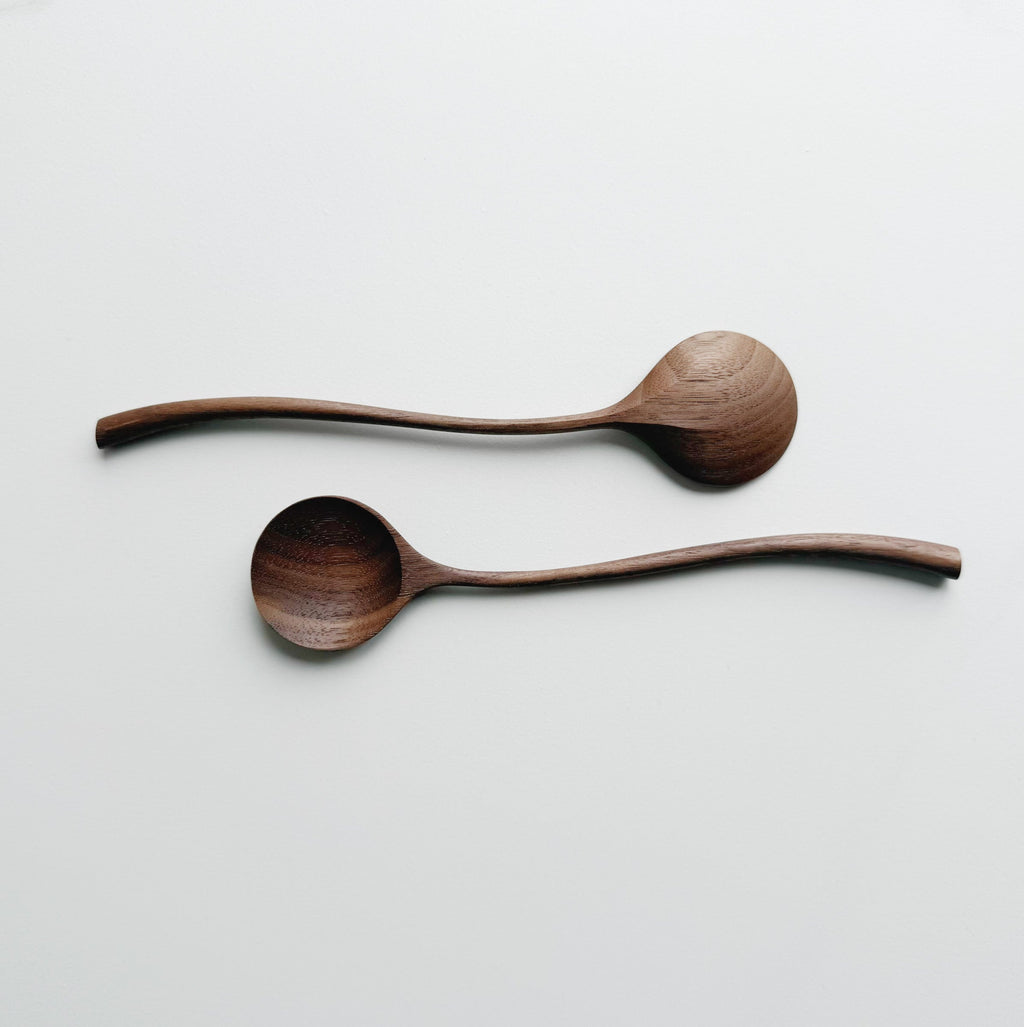 Two walnut curvy spoons on a light background
