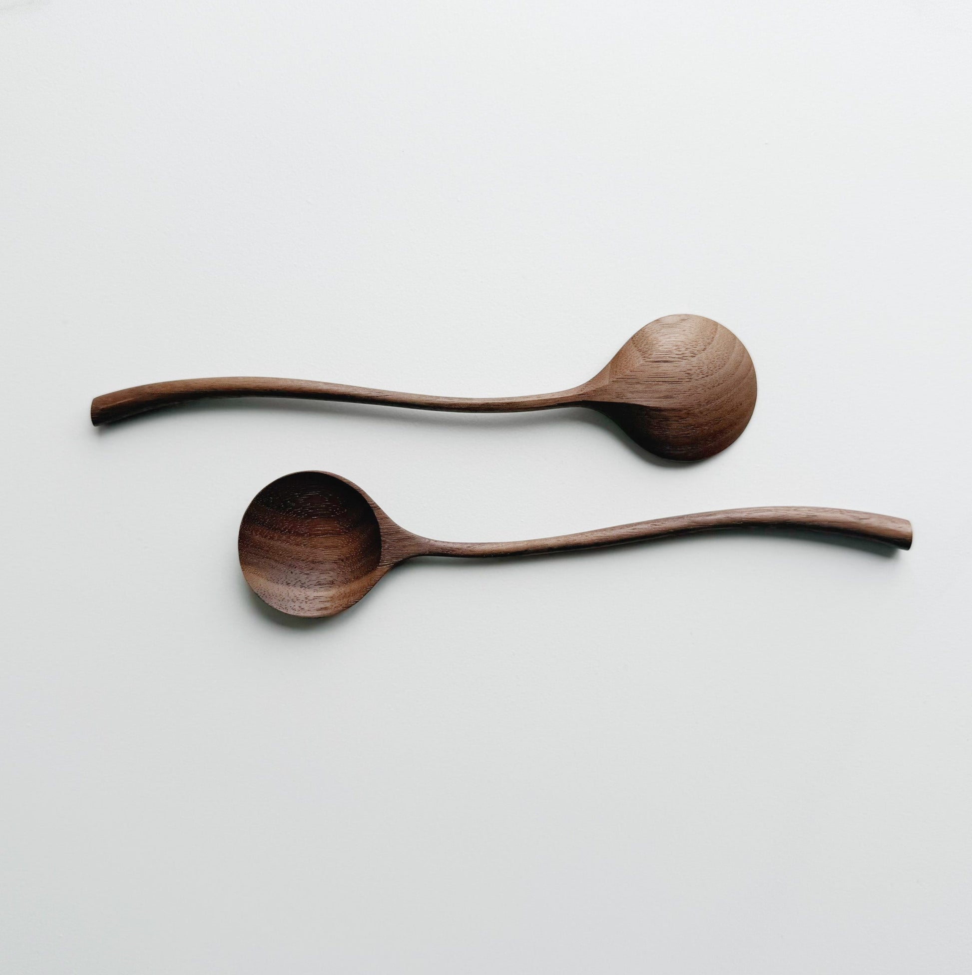 Two walnut curvy spoons on a light background