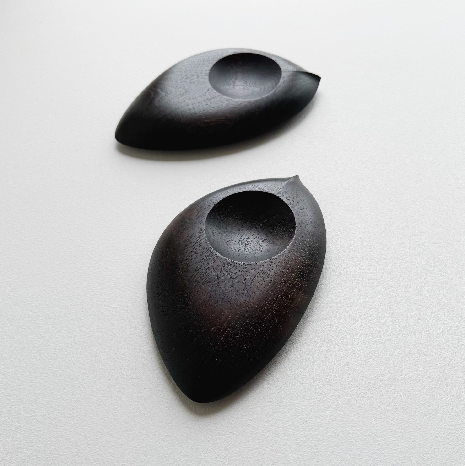 Pair of droplet dishes in ebonised walnut on a light background
