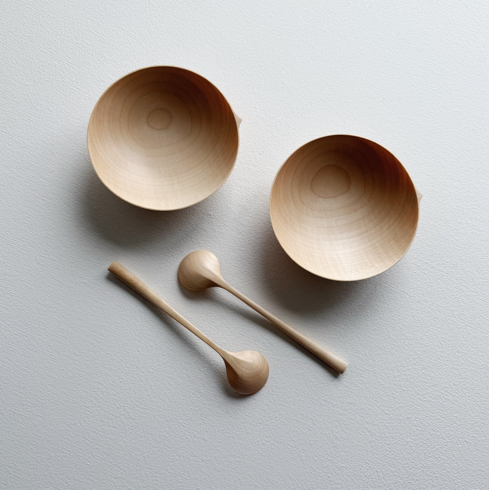 Two sycamore wooden bowls with sycamore spoons on a white background