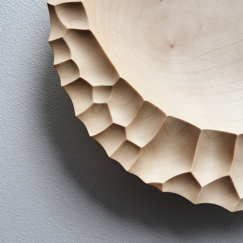 Close up of wooden bowl with sculptural pattern on a white background