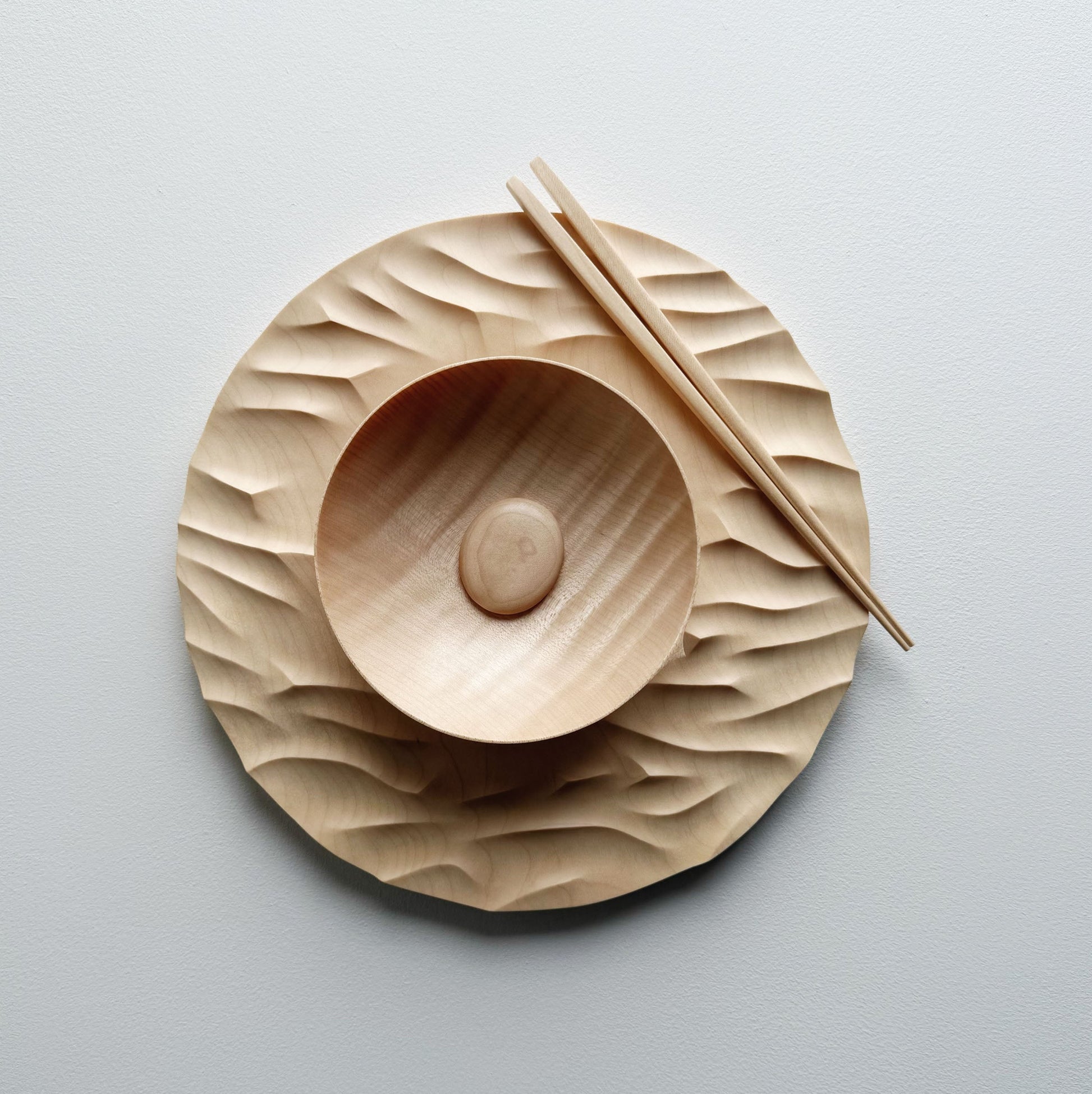 Large Gathered sycamore wooden plate with textured edge and bowl with chopsticks on a light background