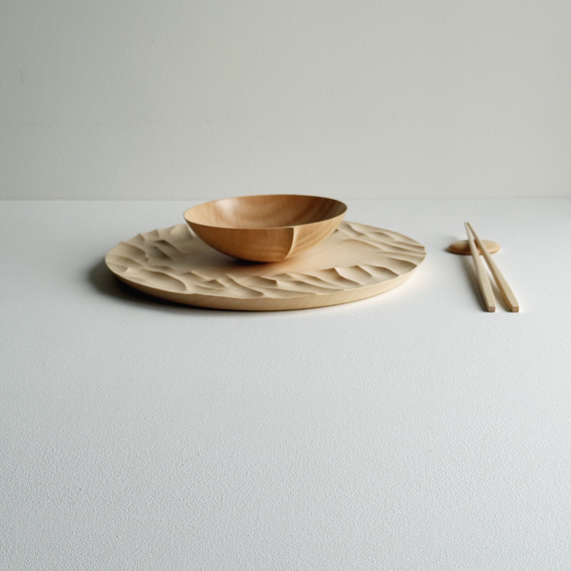 Large Gathered sycamore wooden plate with textured edge and bowl with chopsticks on a light background