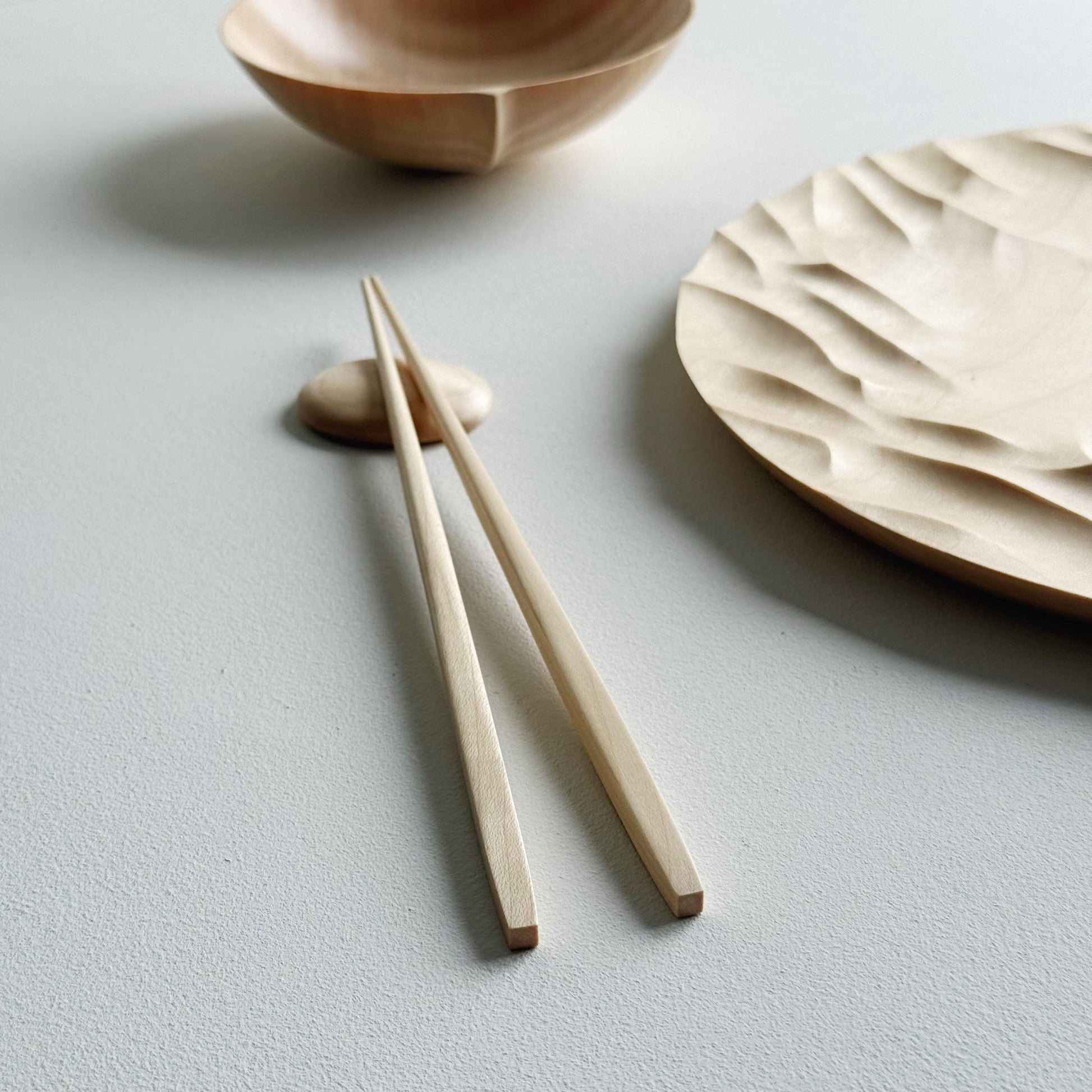 Large Gathered sycamore wooden plate with textured edge and bowl with chopsticks on a light background