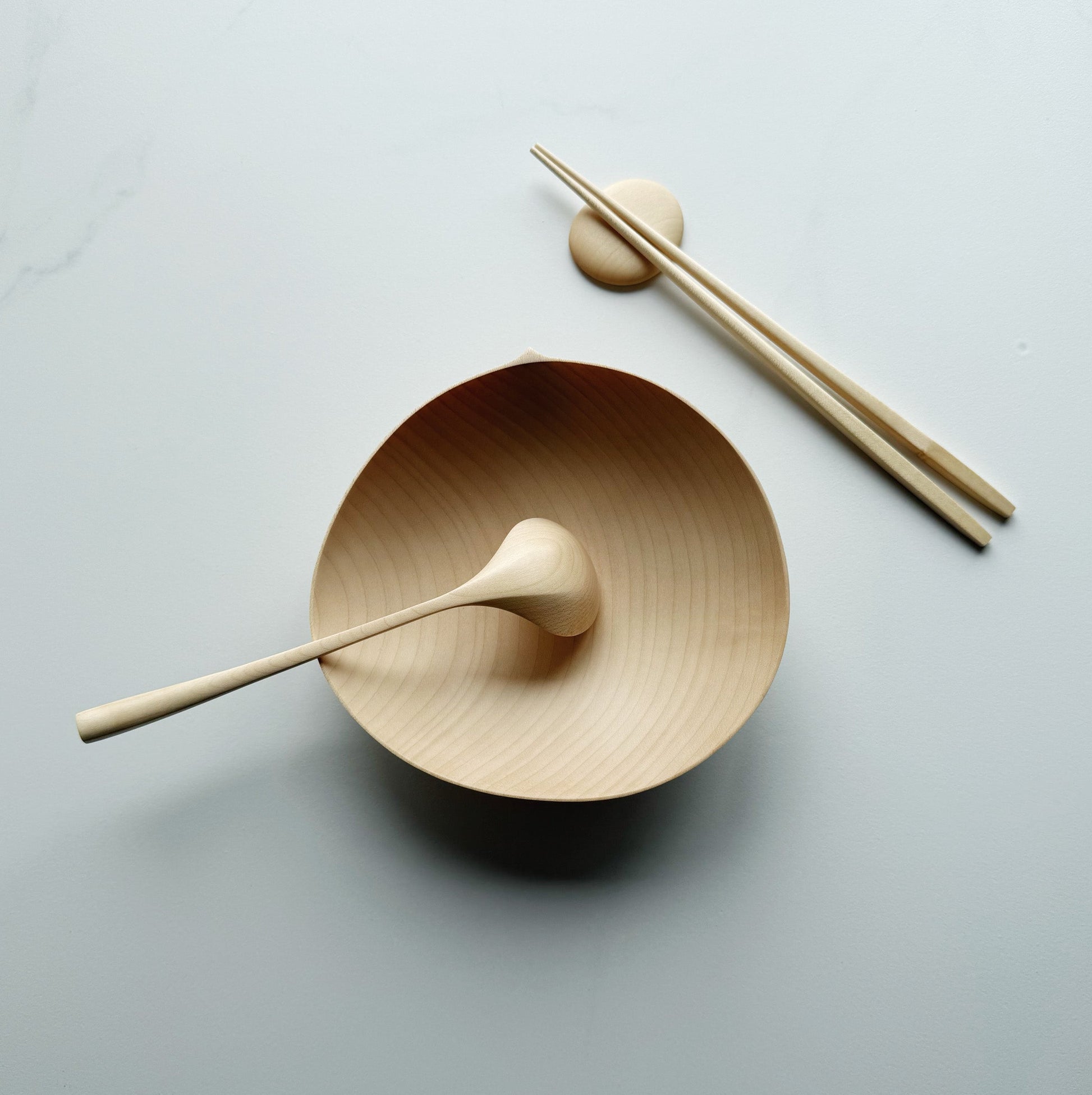 Sycamore oval bowl, angled eating spoon, wooden chopsticks and pebble rests on a white background
