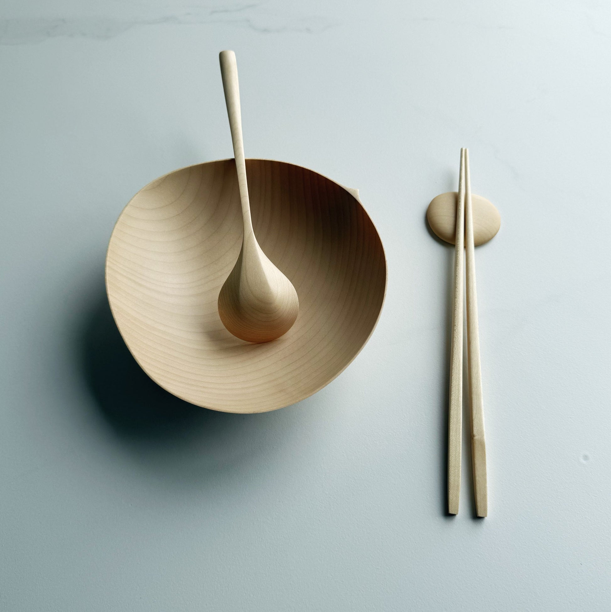 Sycamore oval bowl, angled eating spoon, wooden chopsticks and pebble rests on a white background
