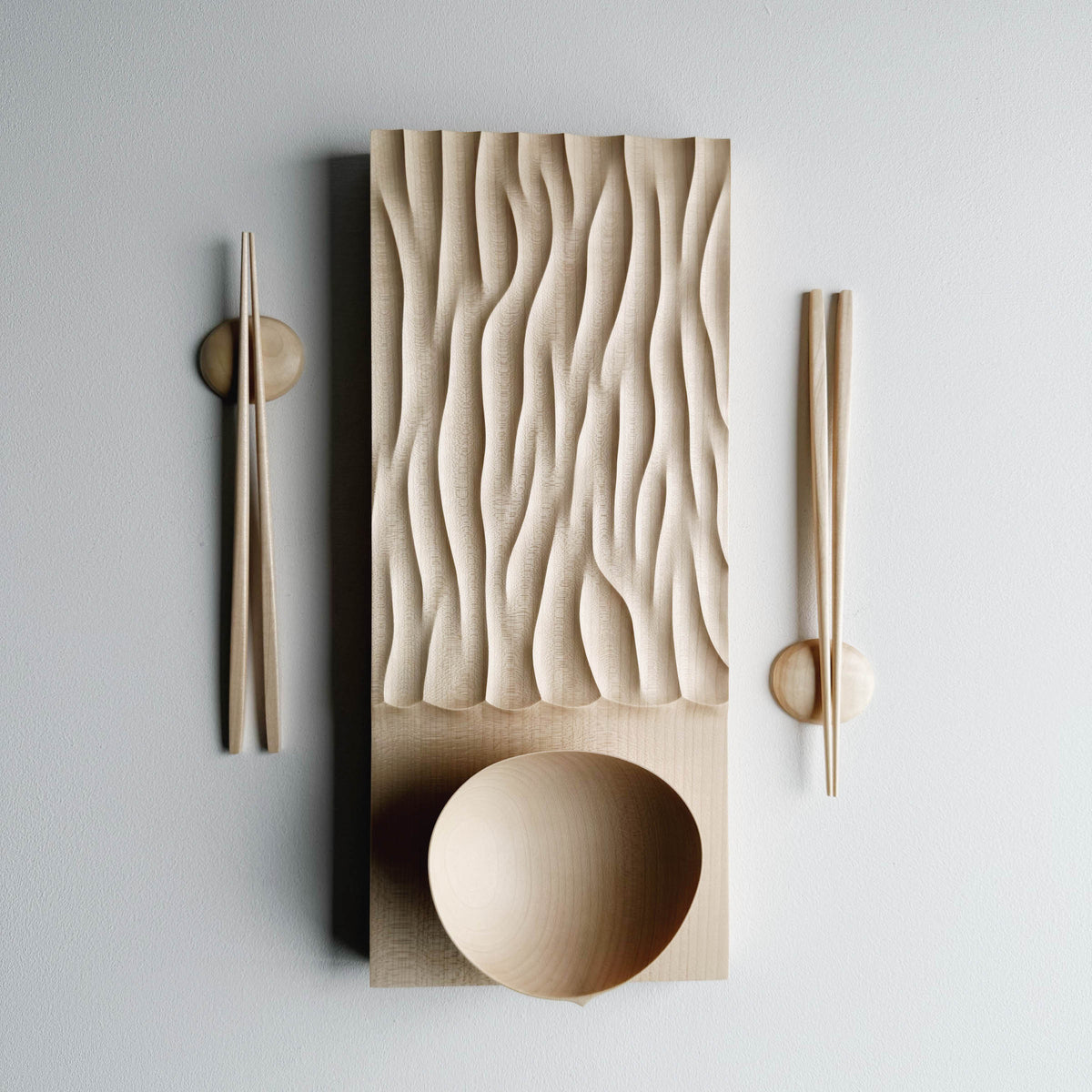 Making Waves sycamore board, with oval bowl, chopsticks and pebble rests in sycamore on a light background.