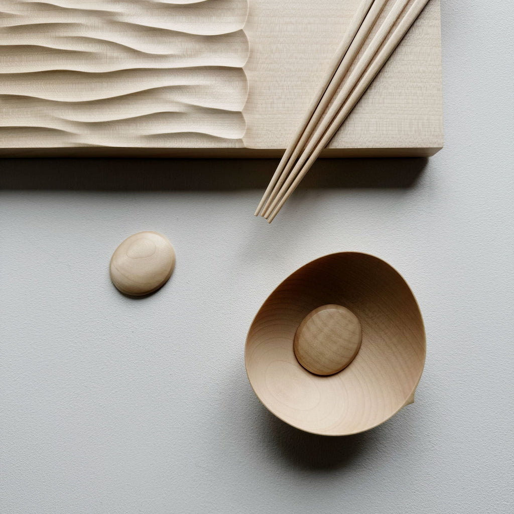 Making Waves sycamore board, with oval bowl, chopsticks and pebble rests in sycamore on a light background.