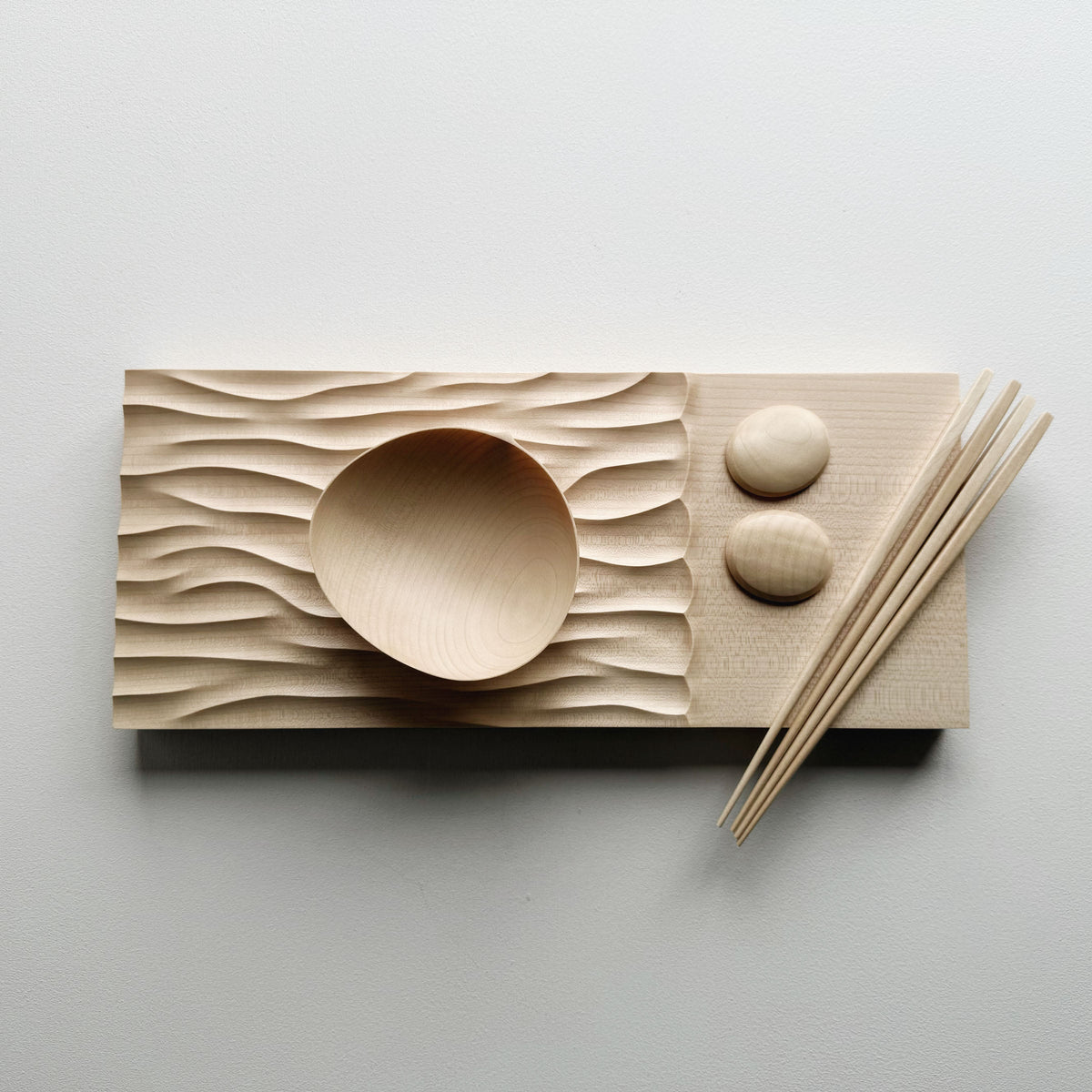 Making Waves sycamore board, with oval bowl, chopsticks and pebble rests in sycamore on a light background.