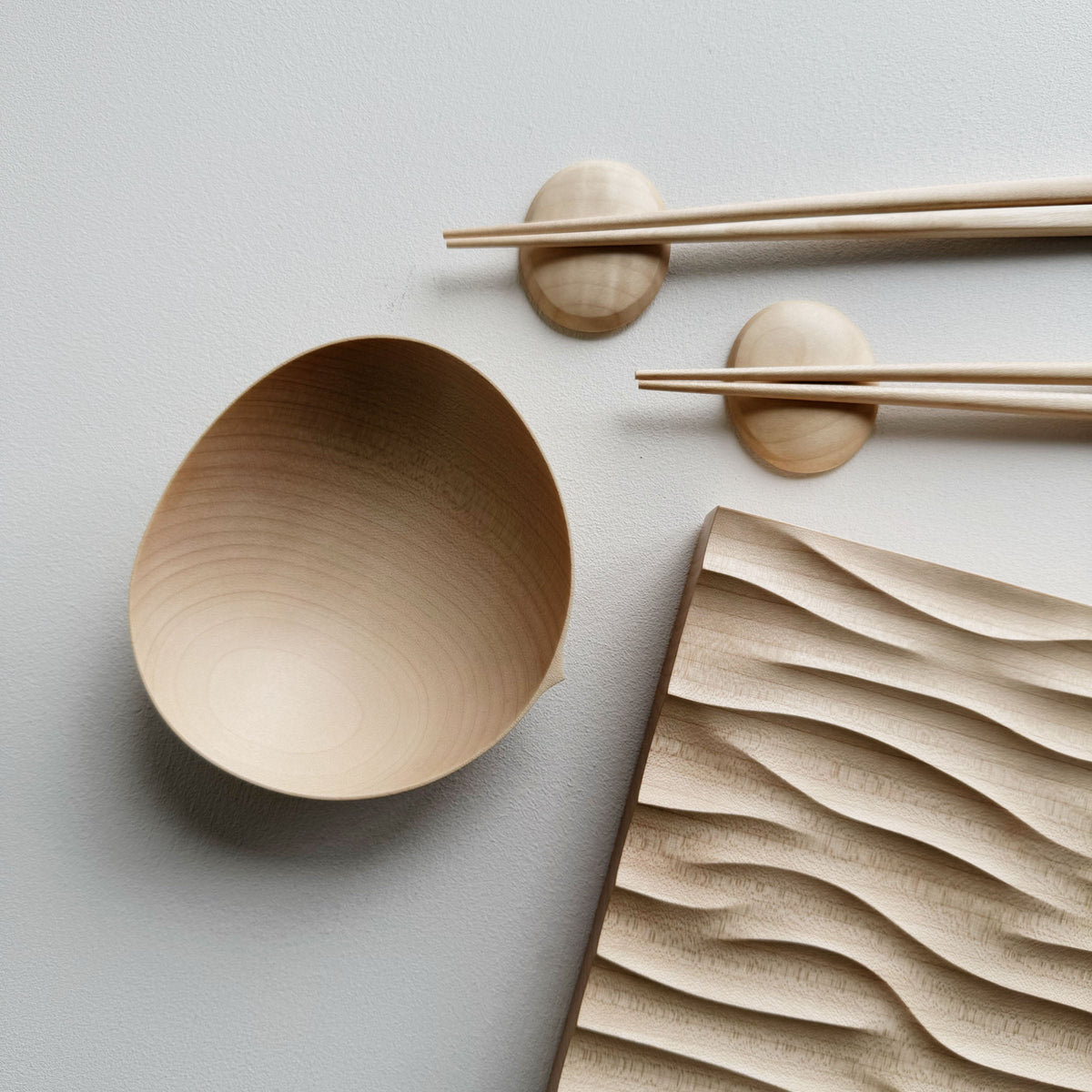 Making Waves sycamore board, with oval bowl, chopsticks and pebble rests in sycamore on a light background.