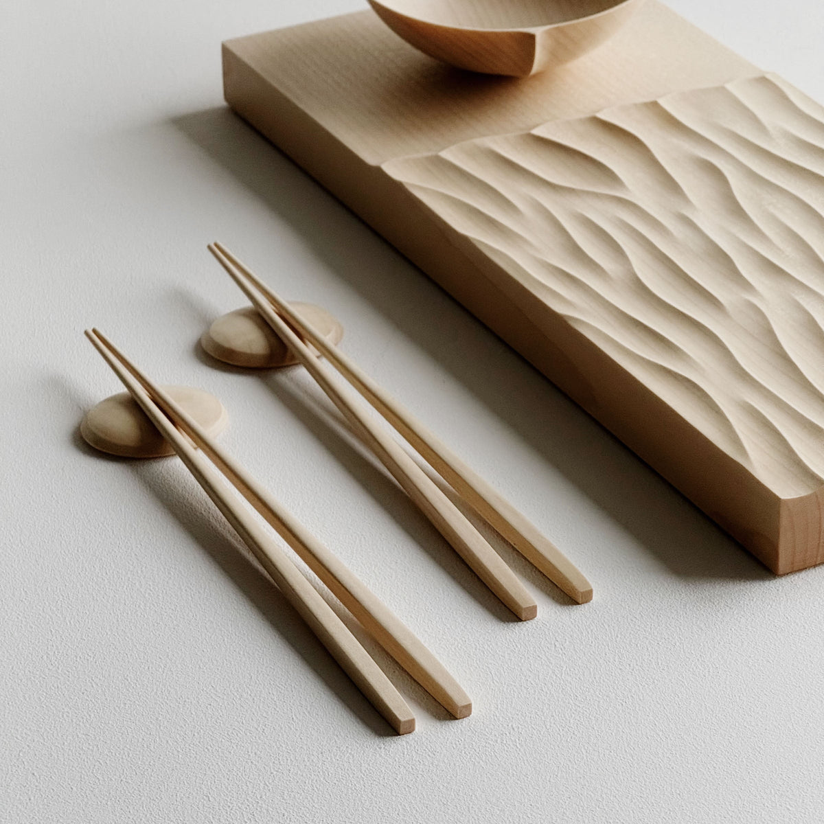 Making Waves sycamore board, with oval bowl, chopsticks and pebble rests in sycamore on a light background.