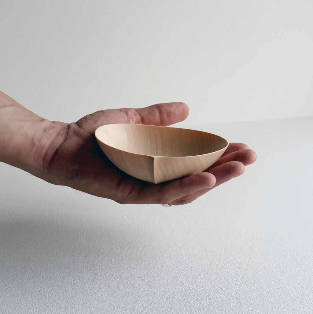 Hand holding an oval palm bowl in sycamore on a white background
