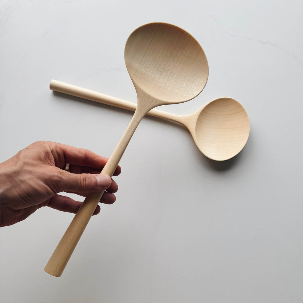 Two large oval servers held by a hand with another spoon on a white background