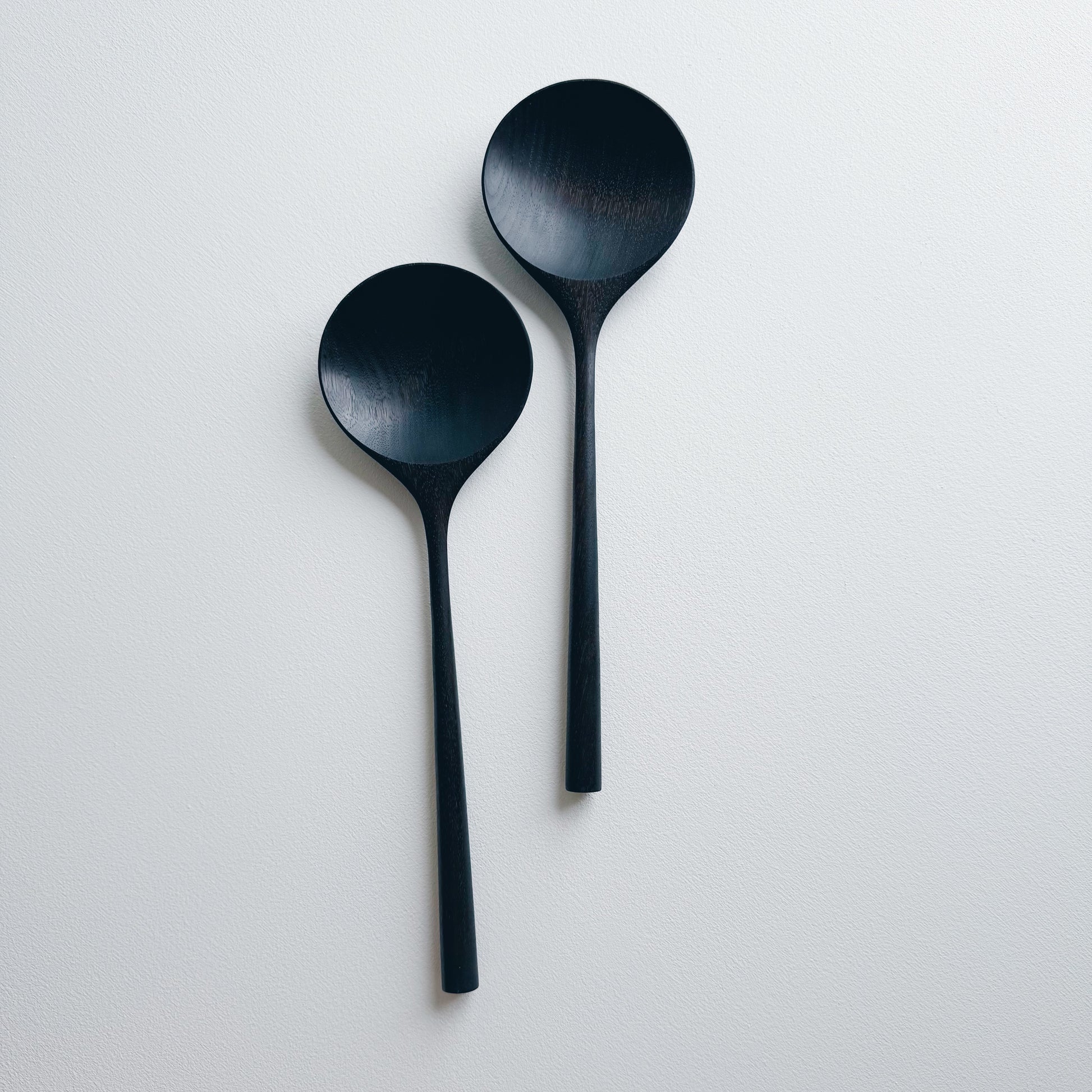 Two ebonised walnut serving spoons on a white background