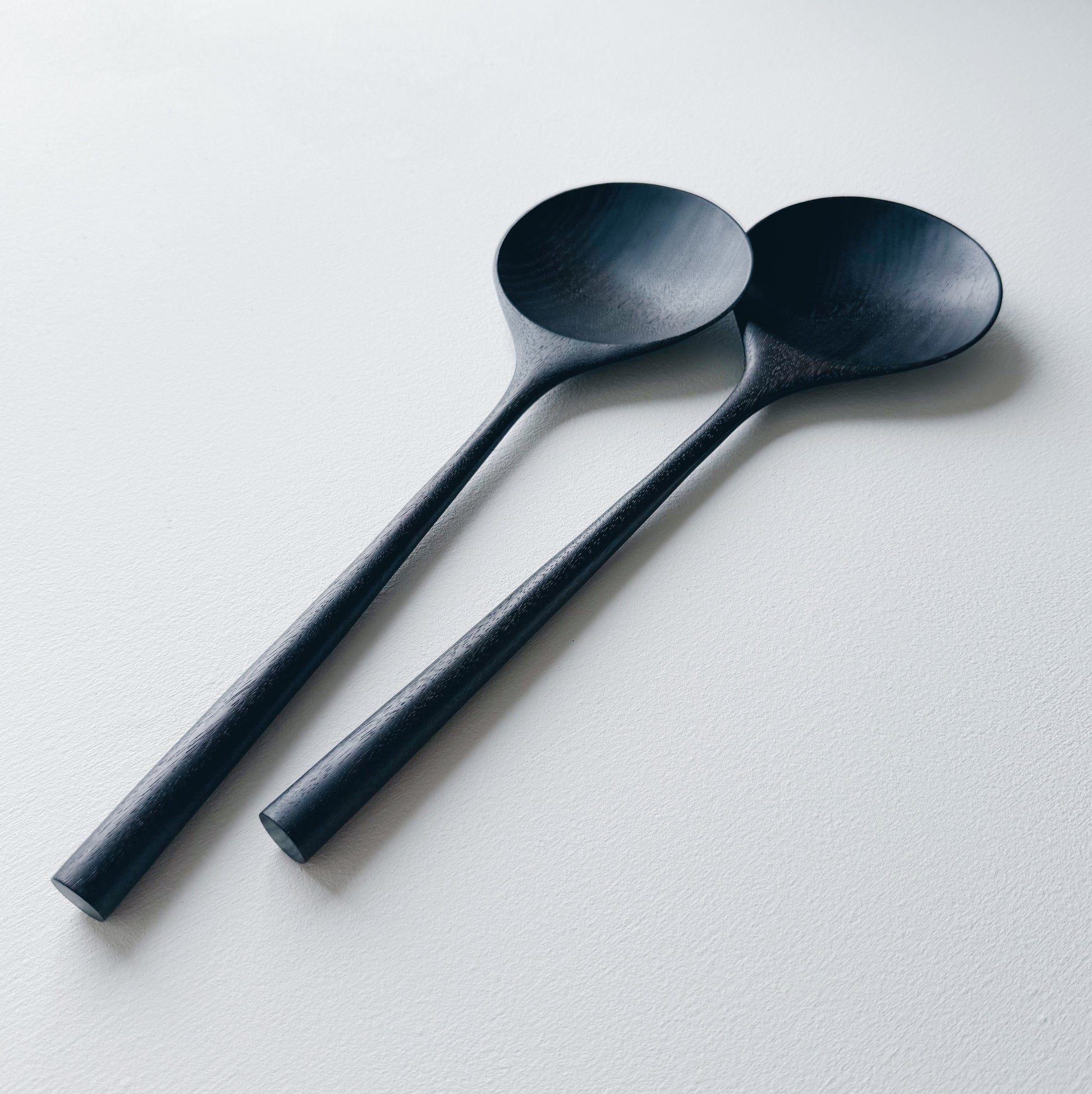 Two ebonised walnut serving spoons on a white background