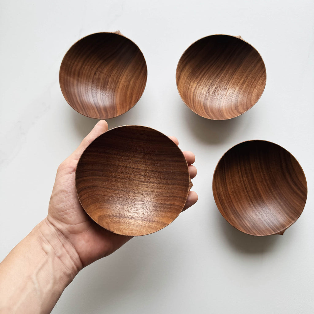 Wooden bowls in walnut on a white background with a hand holding one bowl.