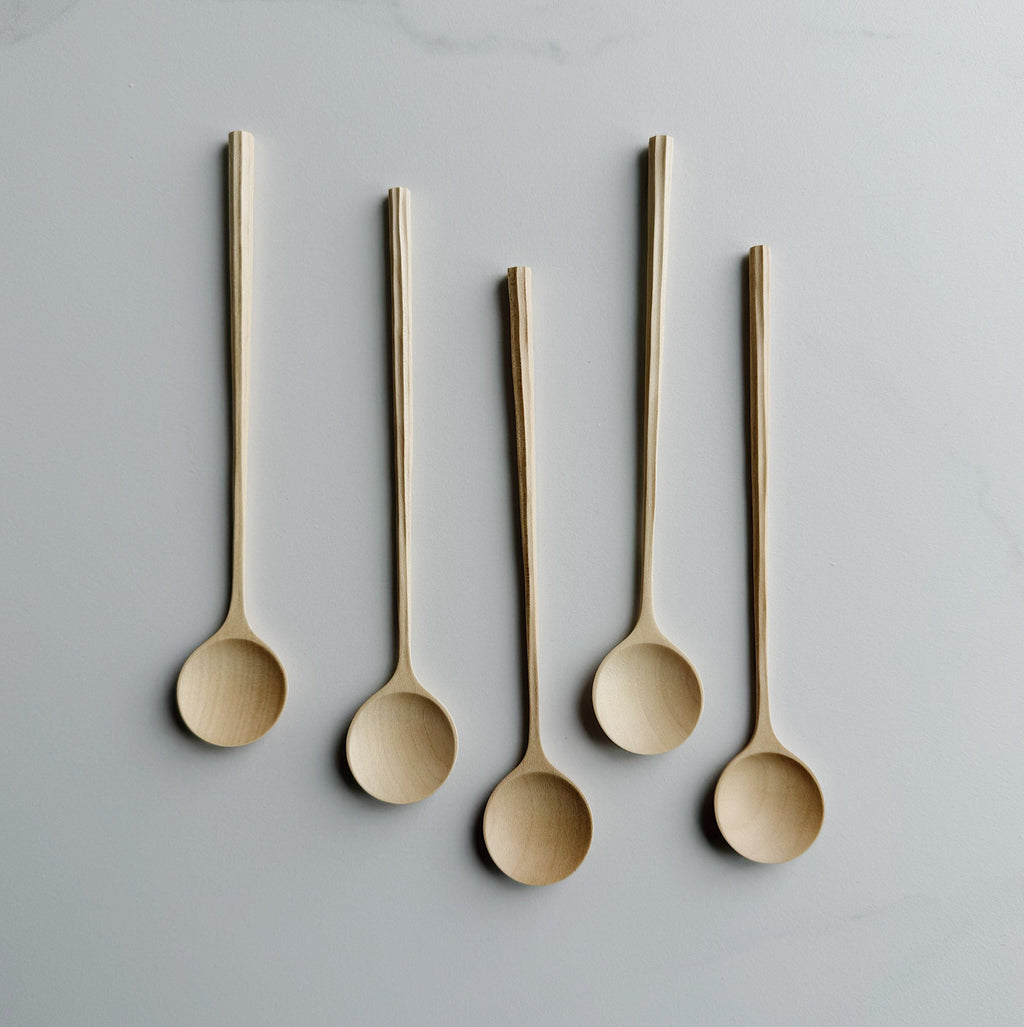 Five sycamore spoons with sculpted handles on a light background