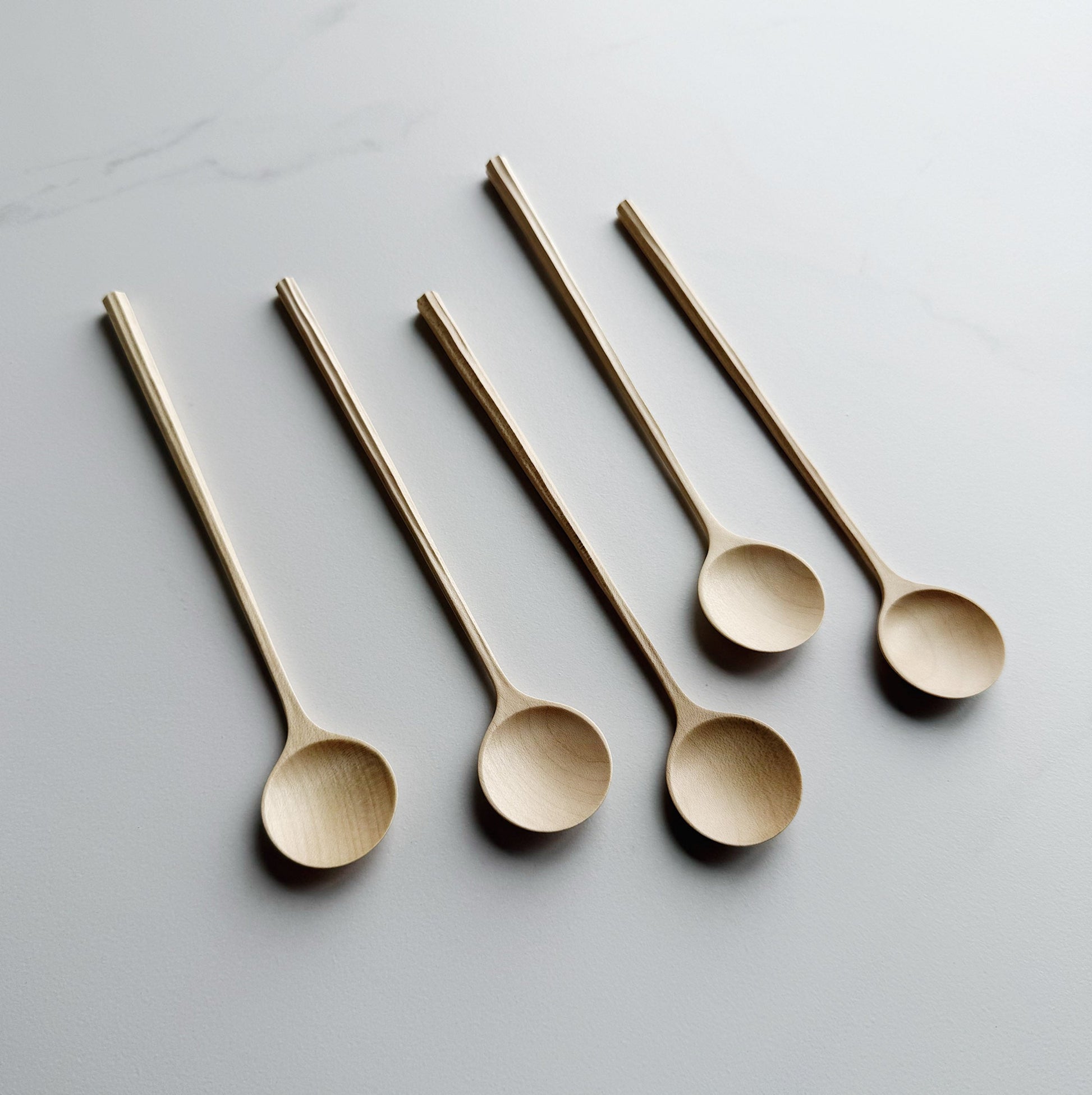 Five sycamore spoons with sculpted handles on a light background