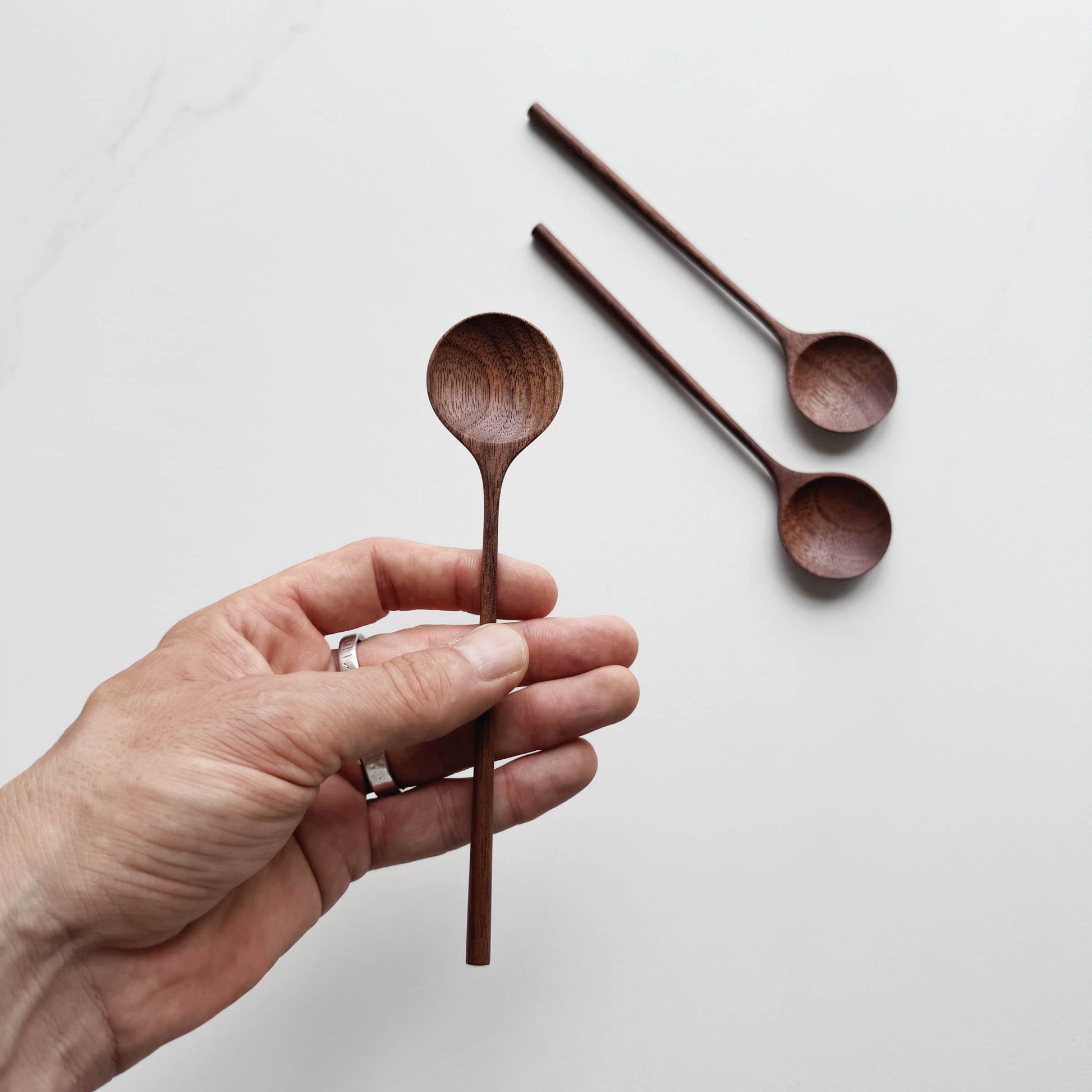 Hand holding a walnut wooden spoon with two other spoons on a light background
