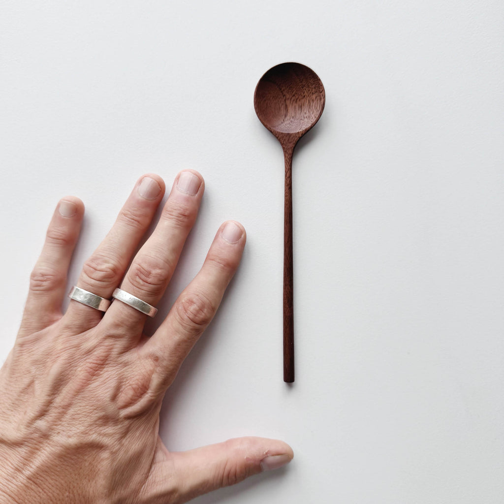 Walnut wooden spoon next to a hand on a light background