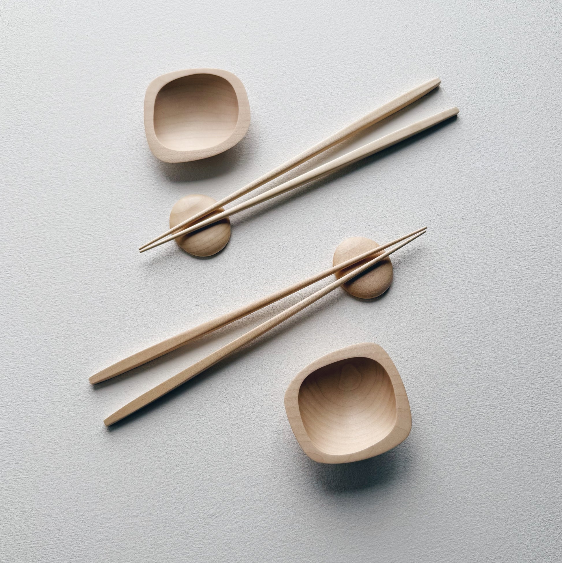 Wavy plates, plinth bowls, chopsticks and pebble rests in sycamore on a light background.