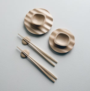 Wavy plates, plinth bowls, chopsticks and pebble rests in sycamore on a light background.