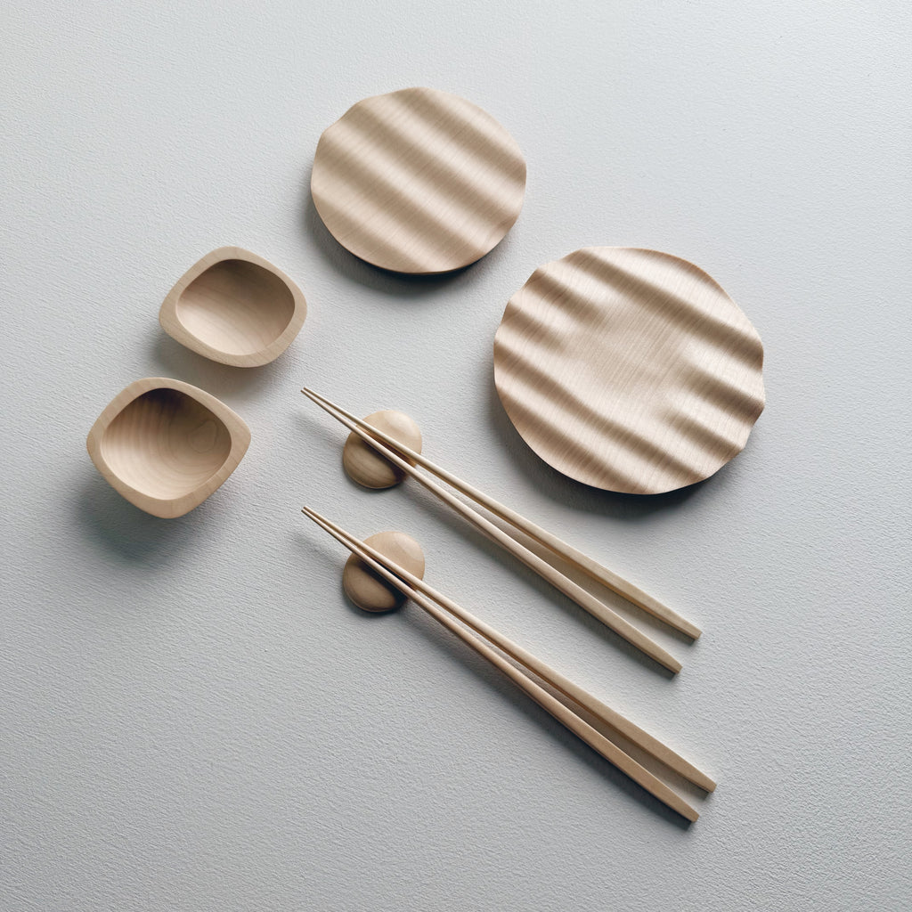 Wavy plates, plinth bowls, chopsticks and pebble rests in sycamore on a light background.