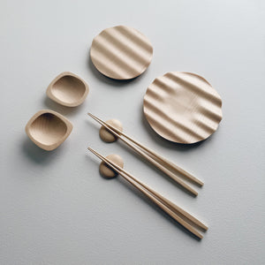 Wavy plates, plinth bowls, chopsticks and pebble rests in sycamore on a light background.