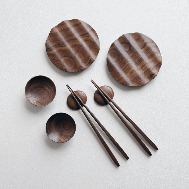 Set of wavy walnut plates and bowls with chopsticks on a light background