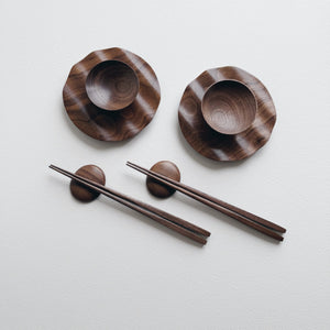 Set of wavy walnut plates and bowls with chopsticks on a light background