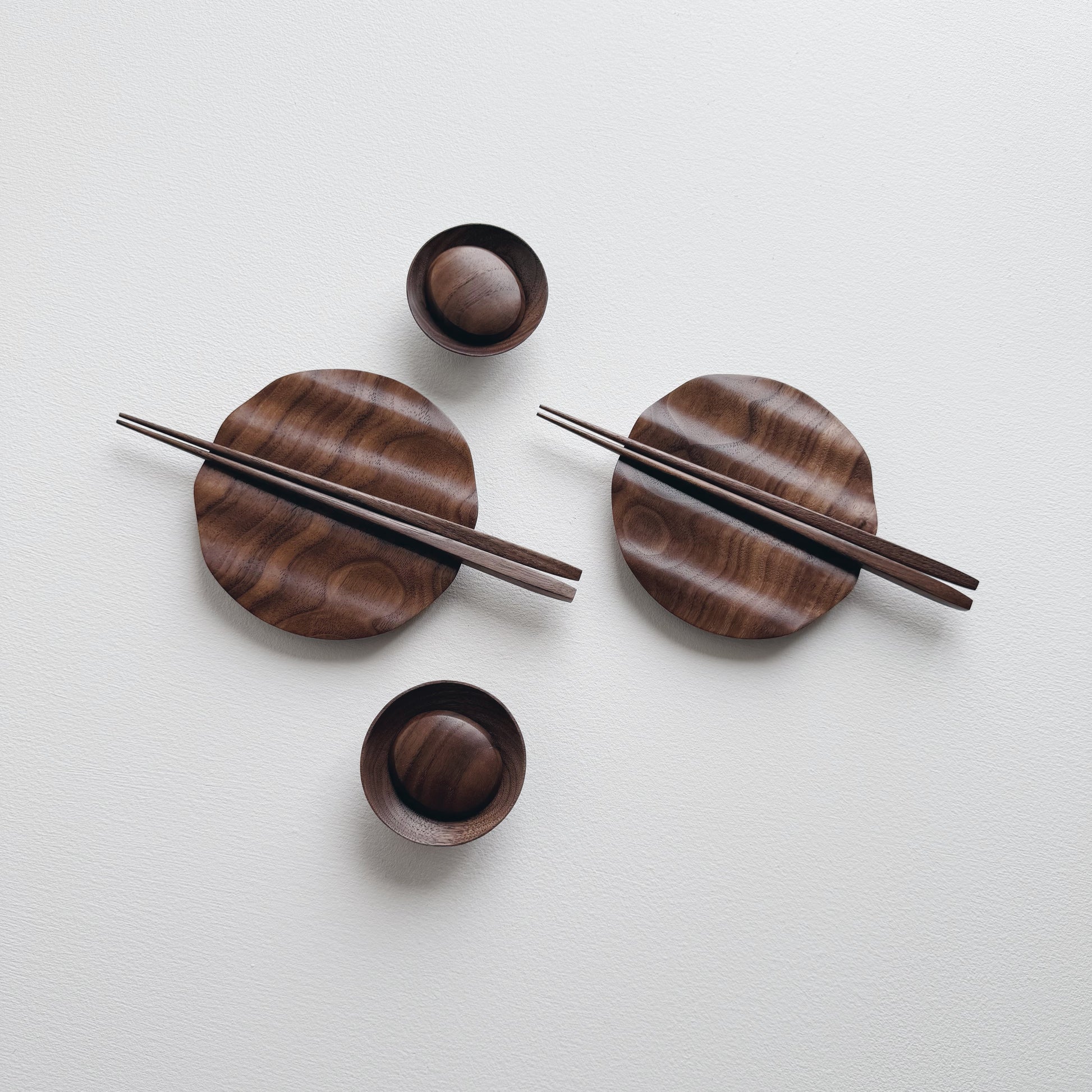 Set of wavy walnut plates and bowls with chopsticks on a light background