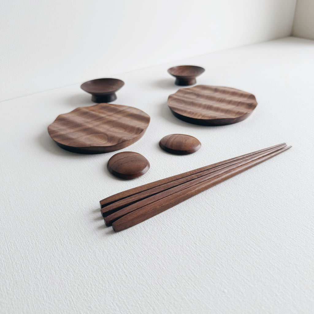 Set of wavy walnut plates and bowls with chopsticks on a light background