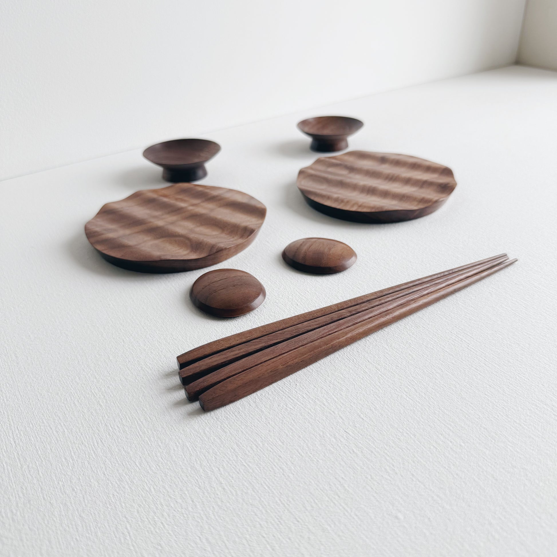Set of wavy walnut plates and bowls with chopsticks on a light background