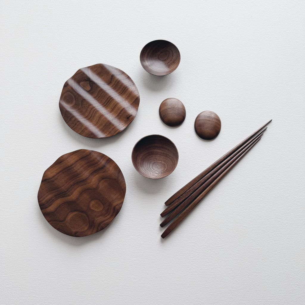 Set of wavy walnut plates and bowls with chopsticks on a light background