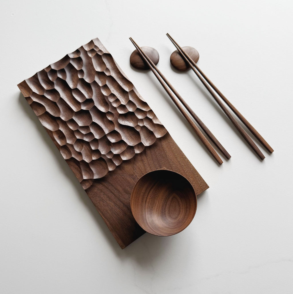 Wide presentation board with crater design in walnut, with a bowl, wooden chopsticks & pebble rests.
