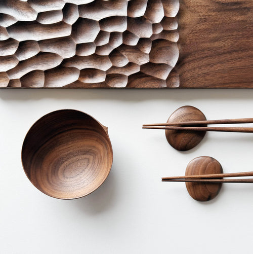 Wide presentation board with crater design in walnut, with a bowl, wooden chopsticks & pebble rests.
