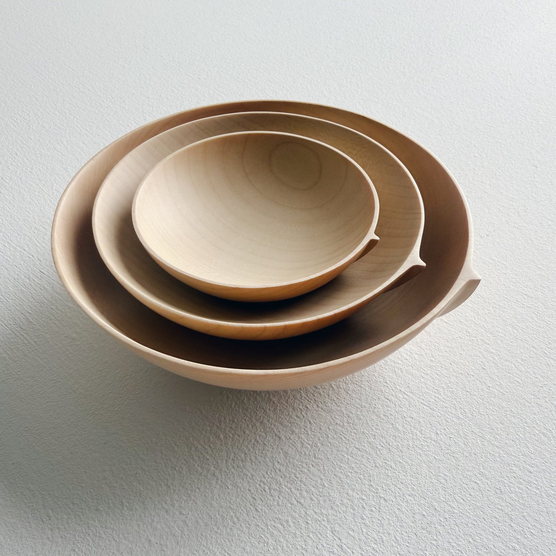 Three sycamore wooden bowls, stacked in nesting formation on a white surface