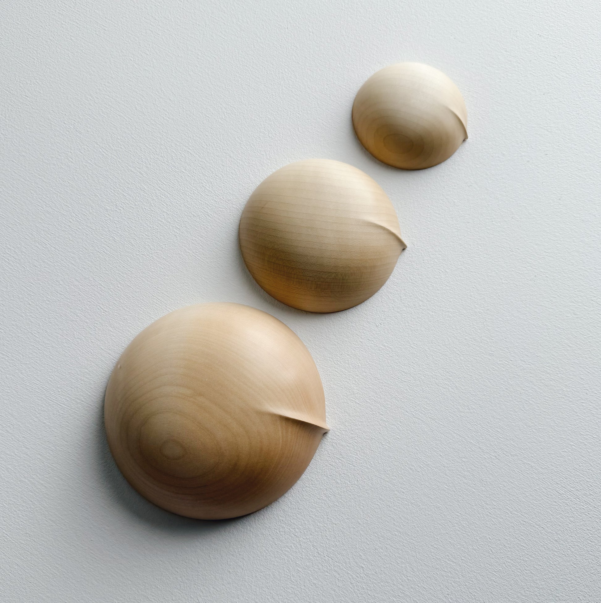Three sycamore wooden bowls, upside down on a white surface
